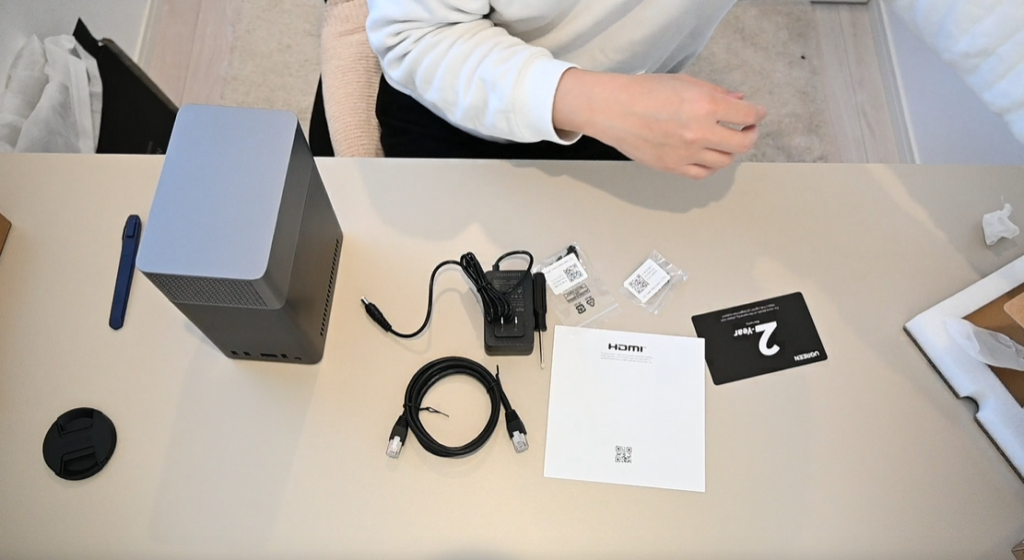 [画像：付属品一覧。本体、ACアダプター、LANケーブル、ネジ類、説明書をデスク上に並べて撮影]