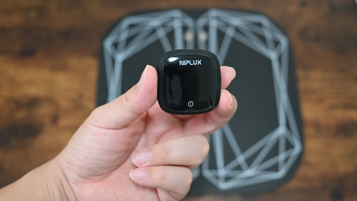 手に持ったNIPLUX LEG FITのコントローラー（NIPLUXロゴと電源ボタン）